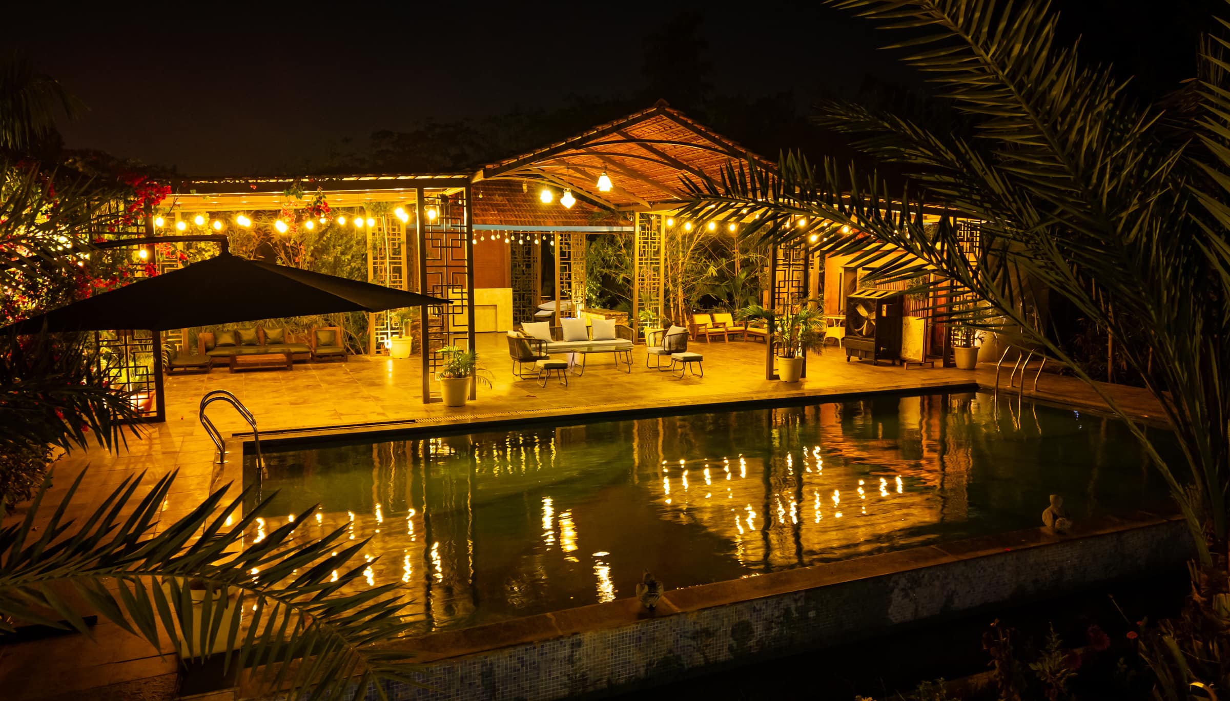 The poolside pergola glowing with string lights after dark, reflected in the water