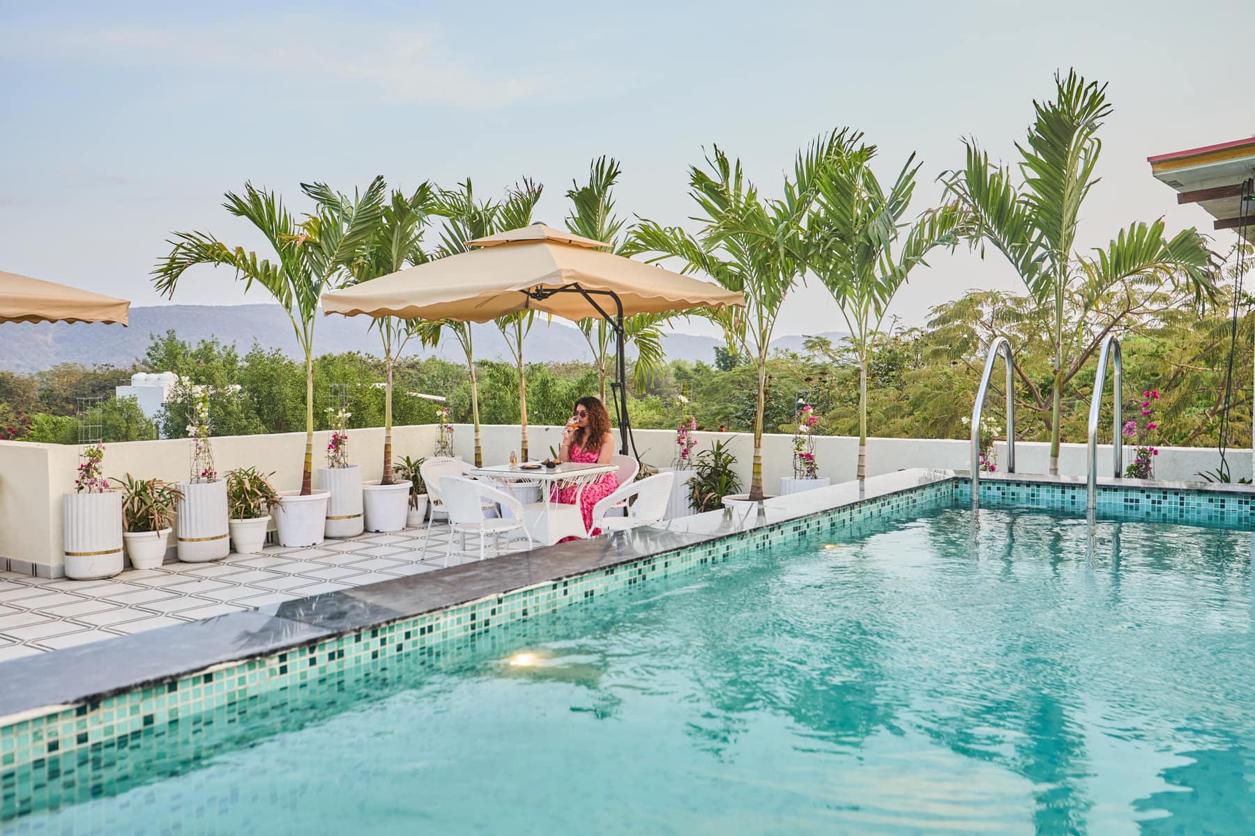 A guest having a drink at a poolside table under a cane umbrella