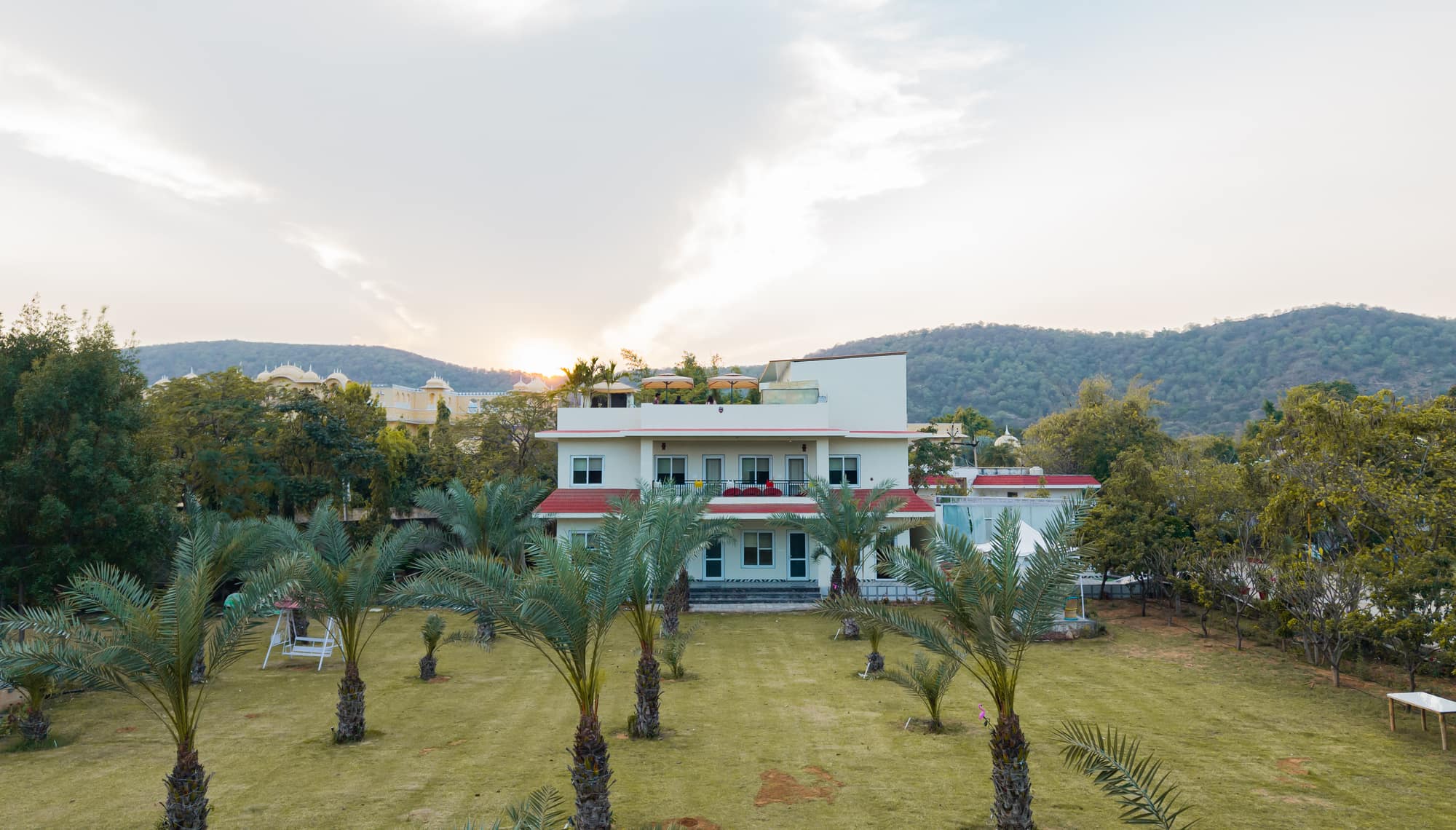 Wild Flower villa across the date-palm lawn at sunset, with the Aravalli hills behind